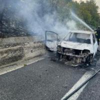 L'auto spenta dopo il rogo e i vigili del fuoco al lavoro per spegnere l'incendio divampato successivamente ai bordi dell'autostrada