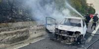 L'auto spenta dopo il rogo e i vigili del fuoco al lavoro per spegnere l'incendio divampato successivamente ai bordi dell'autostrada